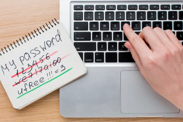 Hand typing a password on a laptop beside a handwritten password note